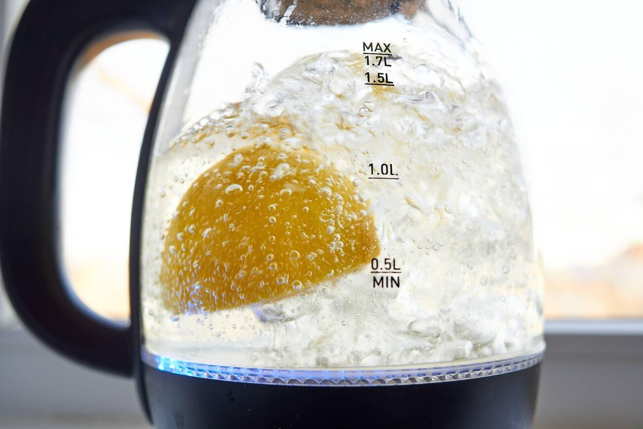 Half a yellow lemon is boiled in a glass electric kettle for descaling